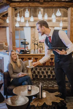 Waiter serving latte to smiling woman in cozy rustic café interior